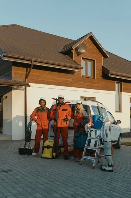A professional cleaner in red coveralls vacuums a contemporary living room with a yellow vacuum cleaner.